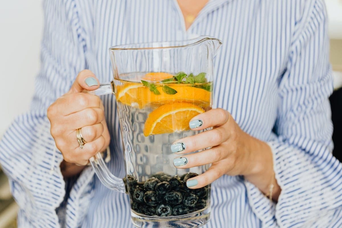 Close-up of infused water with oranges, blueberries, and mint in a glass pitcher.