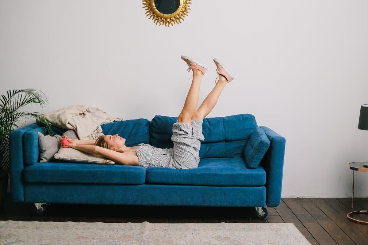 Side view of cheerful young woman with rag and raised legs lying on sofa after housework