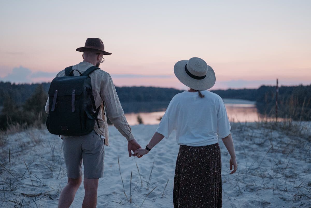 A couple holding hands walking on a sandy beach with sunset views, evoking a sense of love and tranquility.