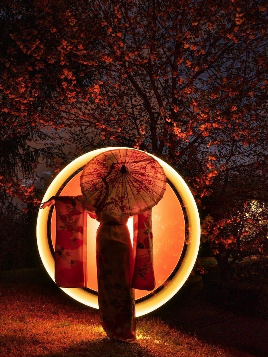 a woman holding an umbrella standing in front of a tree