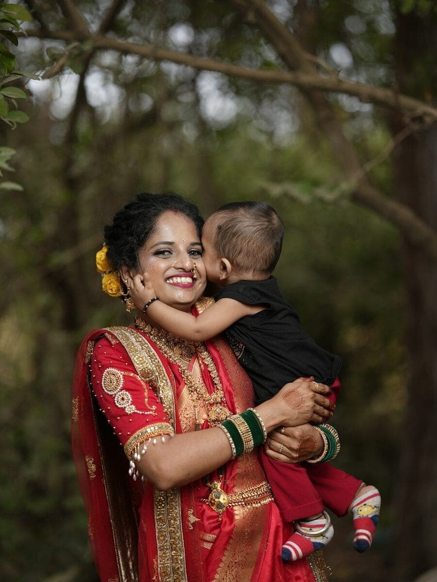 A woman in a red and gold sari holding a baby