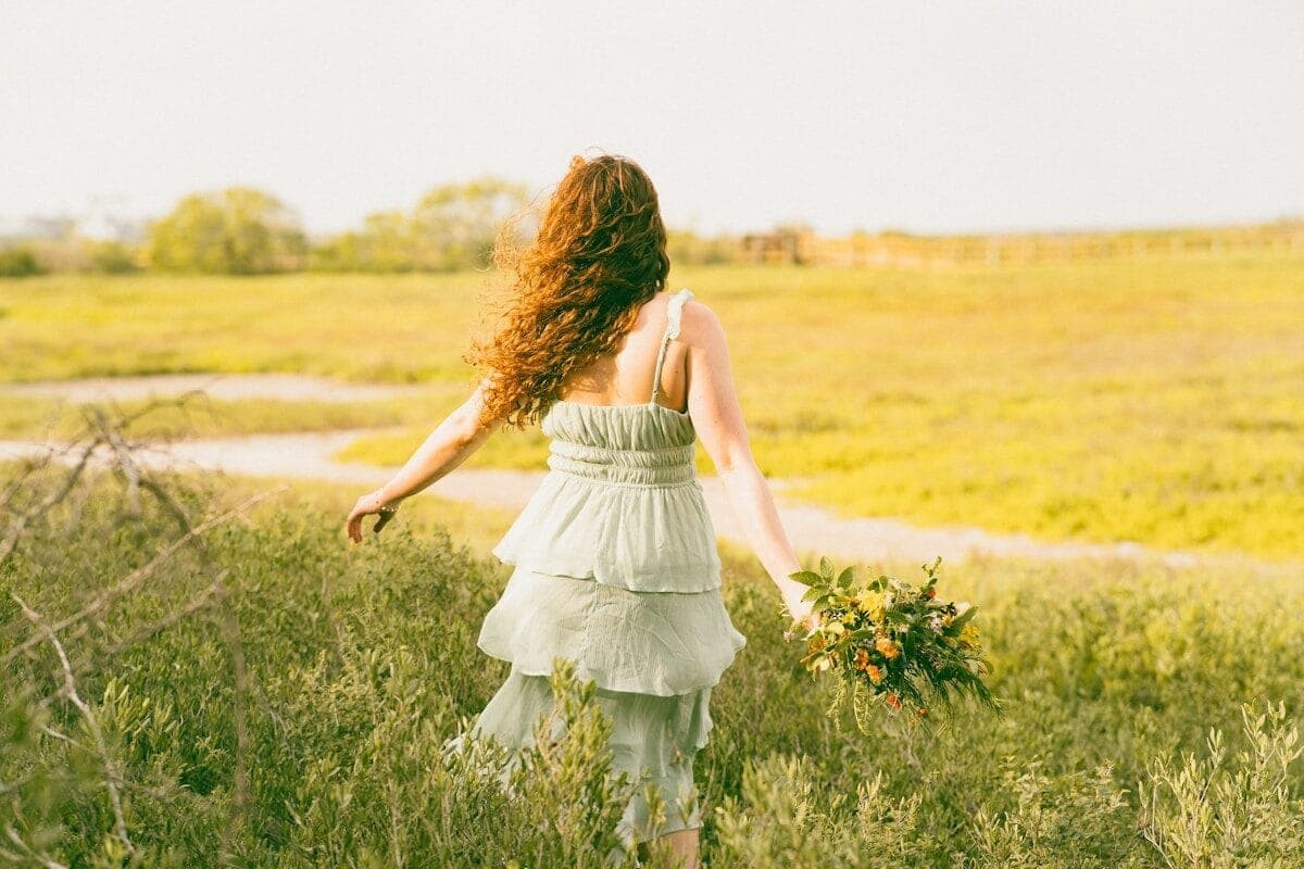 A woman walks away through a grassy field.